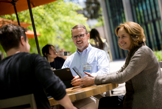 three faculty members talking at a table outside